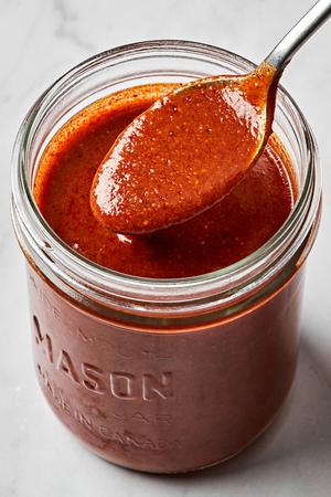 homemade enchilada sauce being spooned out of a glass jar