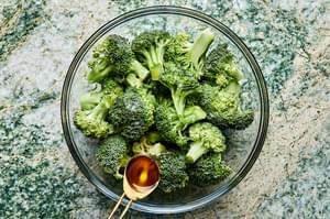 broccoli being tossed with olive oil and salt in a large glass bowl