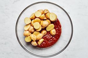 potatoes being tossed with harissa, olive oil, salt, garlic powder, and onion powder in a glass bowl