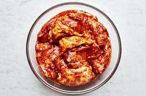 chicken thighs being tossed with harissa, olive oil, salt, garlic powder, and onion powder in a glass bowl