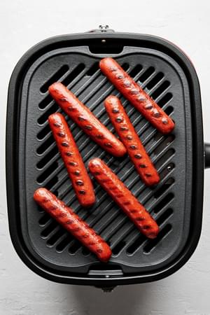 hot dogs cooking on a griddle