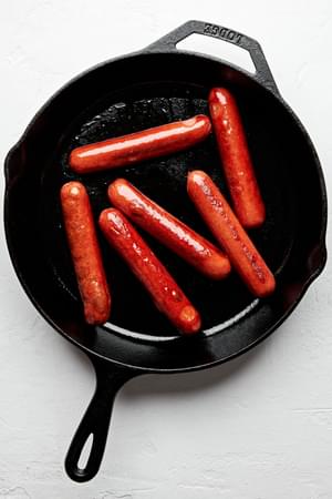 hot dogs being cooked in a cast iron skillet