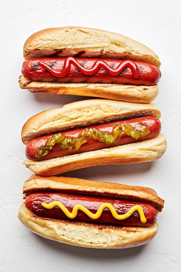3 homemade hot dogs in buns one topped with ketchup, one with mustard and one with relish