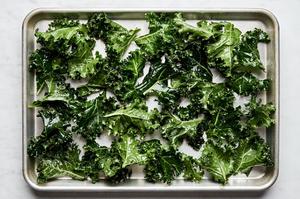 Raw kale leaves, tossed in oil and seasoning, arranged on a baking sheet, ready to be baked into crispy kale chips.