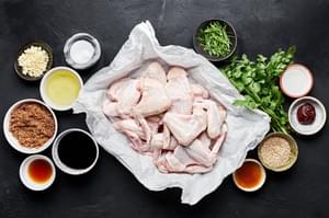 Raw chicken wings next to brown sugar, soy sauce, sesame oil, rice vinegar, fish sauce, green onions and sesame seeds