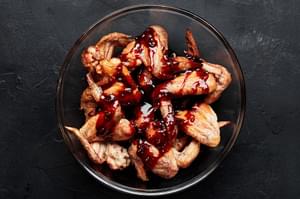 baked chicken wings being tossed in a bowl with homemade kroean style sauce