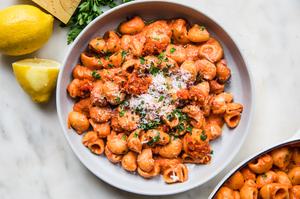 a bowl of homemade lemony calabrian chili pasta topped with parmesan and parsley next to sliced lemons