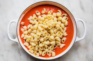 cooked shellbow pasta being added to pan with homemade pasta sauce