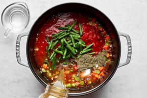 stock, water, tomato sauce, diced tomatoes, green beans and spices being added to a soup pot with cooked vegetables
