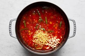 cannellini beans and pasta being added to a soup pot with other ingredients for minestrone soup