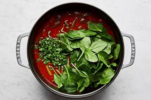 fresh basil and spinach being added to a pot of homemade minestrone soup