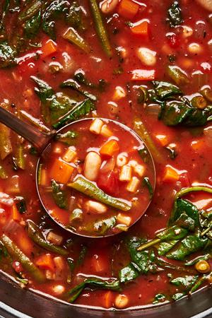 a ladle in a pot of homemade minestrone soup made with pasta, cannellini beans, green beans, carrots, celery and onion