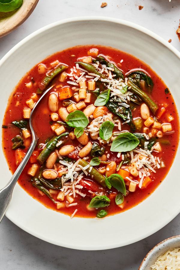 homemade minestrone soup topped with parmesan cheese and fresh basil in a bowl with a spoon in it