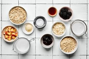 ingredients laid out to make overnight oats: oats, coconut milk, chia seeds, jam, fruit, protein powder and maple syrup