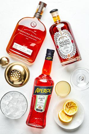 bourbon, amaro Nonino, Aperol, fresh lemon juice, ice, coupe glass and a cocktail shaker on the counter for a paper plane