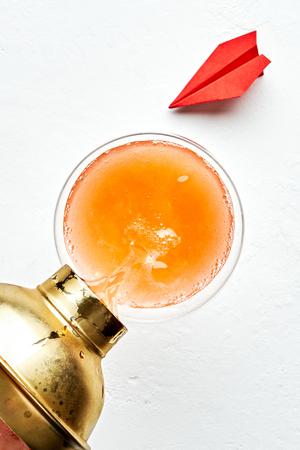 a paper plane cocktail being poured into a coupe glass from a cocktail shaker