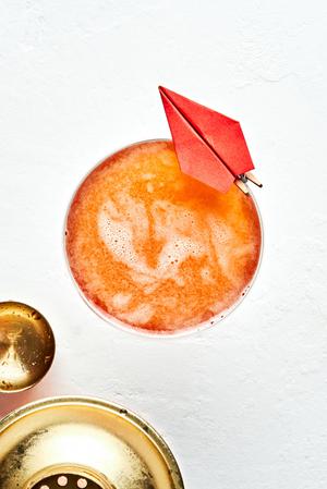 a paper plane cocktail in a coupe glass with a small paper airplane attached to the side of the glass