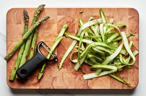 asparagus being peeled into ribbons with a vegetable peeler on a cutting board