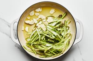 asparagus ribbons and thinly sliced garlic being cooked in olive oil in a skillet