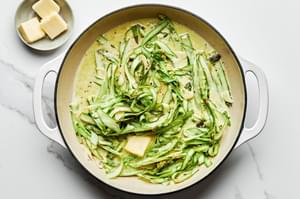 butter being added into a pan with olive oil, asparagus ribbons, garlic, pepper, lemon zest, heavy cream & salt