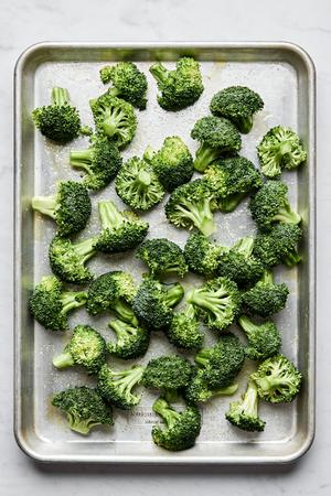 raw broccoli tossed with olive oil, salt and pepper on a baking sheet