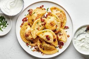 homemade pierogi potato dumplings cooked with bacon & onion on a serving plate next to bowls of cottage cheese and sour cream