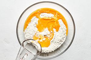 water being poured into a bowl with flour, salt and eggs to make a dough for pierogis