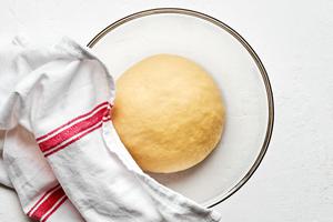 pierogi dough in a glass bowl made with flour, water, salt and oil being covered with a damp towel to allow the dough to rest