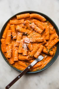 pink sauce Tortiglioni in a bowl with a fork, sprinkled with grated parmesan cheese and fresh chopped basil