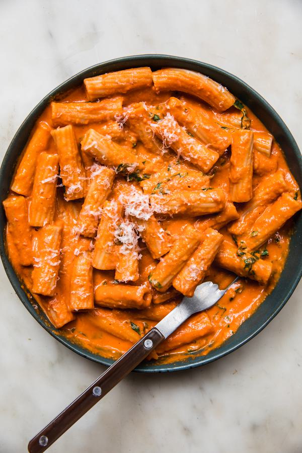 pink sauce Tortiglioni in a bowl with a fork, sprinkled with grated parmesan cheese and fresh chopped basil