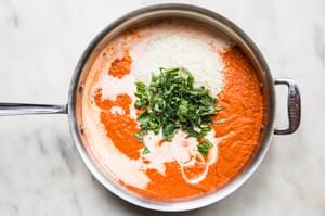 cream, parmesan and basil being added to a pan with blended pasta sauce