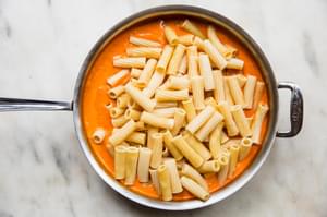 cooked tortiglioni pasta noodles being stirred in a pan with pink pasta sauce