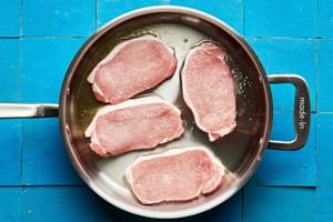 4 1/2-inch thick pork chops being browned in olive oil in a skillet