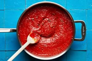 tomato sauce made with olive oil, garlic, tomatoes, pepper, basil, parmesan, sugar, and vinegar cooking in a skillet