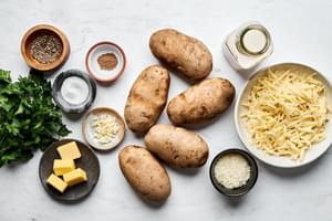 ingredients laid out for potatoes au gratin: butter, cream, garlic, nutmeg, potatoes, salt, pepper, Gruyère, Parm & parsley