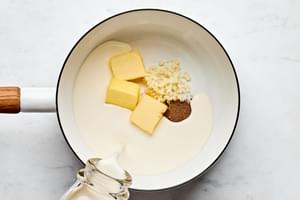 rich sauce being made in a pot with heavy cream, garlic, nutmeg, and butter to use in a potatoes au gratin recipe.