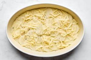 Layering creamy potatoes au gratin in a casserole dish, with thin slices of potato and rich cheese sauce.
