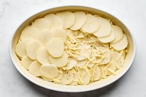 Layering creamy potatoes au gratin in a casserole dish, with thin slices of potato and rich cheese sauce.