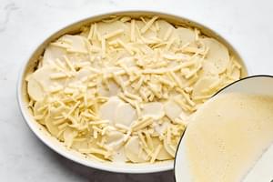 Layering creamy potatoes au gratin in a casserole dish, with thin slices of potato and rich cheese sauce.