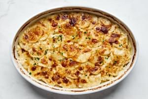 A casserole dish filled with golden, creamy potatoes au gratin, topped with a crispy cheese layer garnished with parsley.
