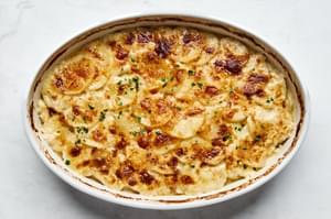 A casserole dish filled with golden, creamy potatoes au gratin, topped with a crispy cheese layer garnished with parsley.
