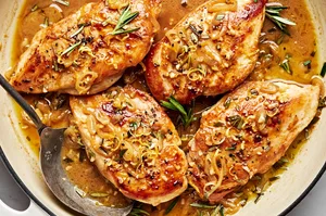 homemade rosemary chicken in pan made with butter, shallots, garlic, rosemary, dijon, lemon juice & zest with a serving spoon