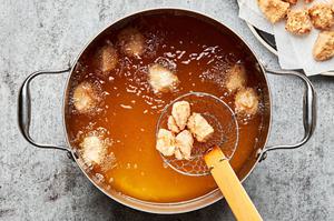 chicken bites breaded in egg, flour and corn starch being deep fried in a pot of vegetable oil