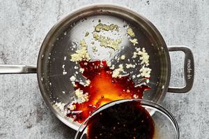 sesame oil sauce being added to a skillet with garlic and ginger