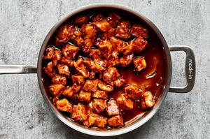 deep fried chicken bites being tossed in homemade sesame sauce in a skillet