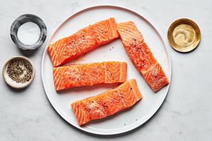 four 4 ounce salmon filets on a plate surrounded by bowls of salt, pepper and garlic powder to use for seasoning
