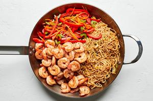 shrimp, chow mein noodles, cooked bell peppers, carrots, celery, onion amd cabbage being tossed together in a skillet