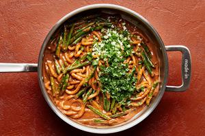 green onions and cilantro being added to spicy peanut noodles and green beans in a pan