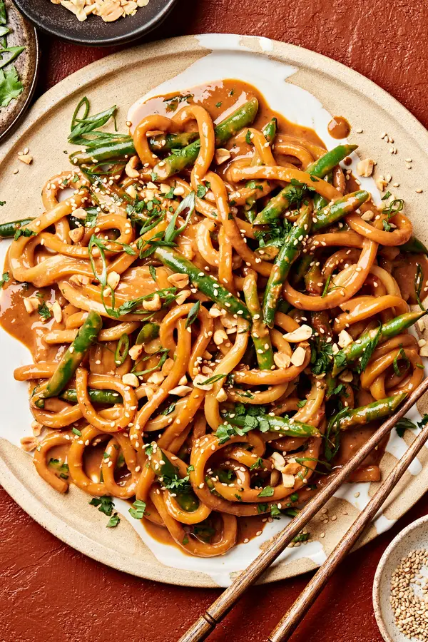 homemade spicy peanut udon noodles topped with green onions, cilantro, sesame seeds, and crushed peanuts on a plate