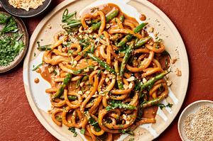 homemade spicy peanut udon noodles topped with green onions, cilantro, sesame seeds, and crushed peanuts on a plate
